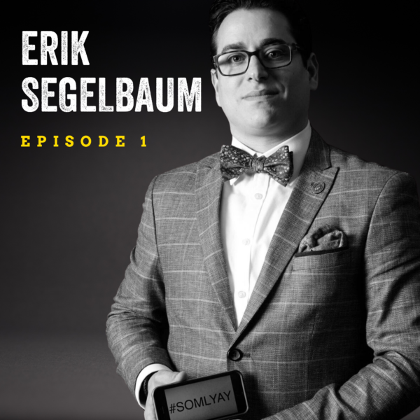 Black and white image of a man wearing a plaid jacket and bowtie, with glasses and short dark hair. He is in front of a dark background with text overlay reading "Erik Segelbaum Episode 1."