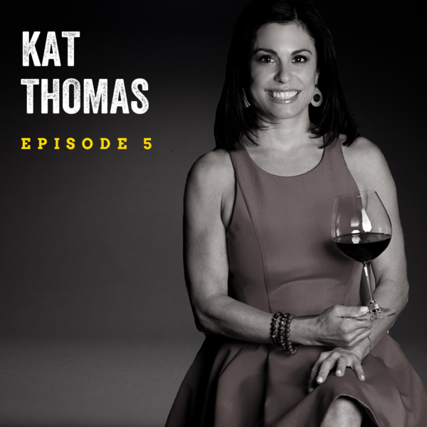 Black and white image of a woman seated and holding a glass of red wine. She has dark medium length hair and a bright smile, and wears a cocktail dress. The background is dark and text overlay reads "Kat Thomas Episode 5."