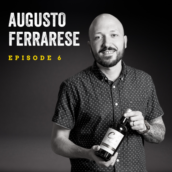Black and white image of bald man with a dark beard holding a bottle of wine with both hands. The background is dark and the text overlay reads: "Augusto Ferrarese Episode 6."