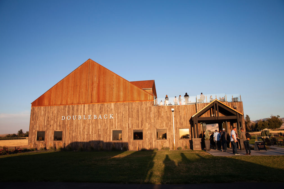 Large barn-like structure with natural wood siding and the words "Doubleback" on the side. Background is a periwinkle blue sky.
