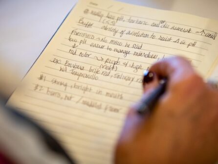 A hand holding a pen rests above a page with hand-written notes.