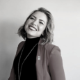 black and white image of a woman (Jennifer Estevez) with shoulder-length hair smiling at the camera, wearing a blazer with a sommelier pin and dark turtleneck