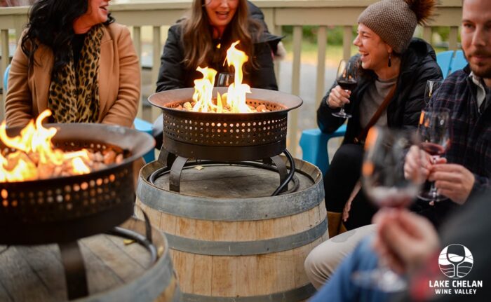 A group of people sitting around a fire pit laughing and drinking wine.